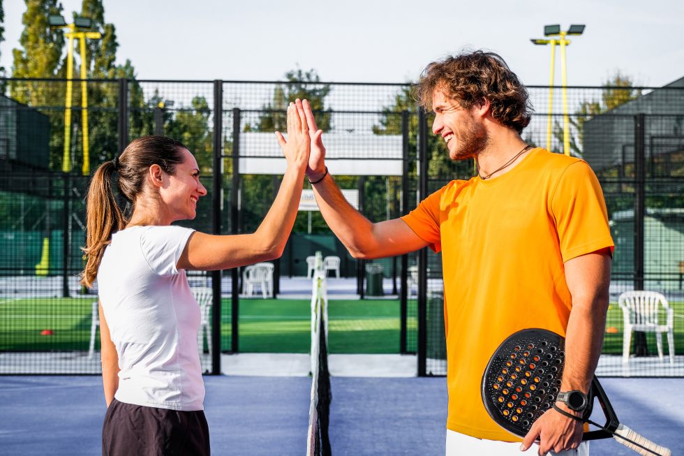 A couple playing padel together on court, laughing during a rally