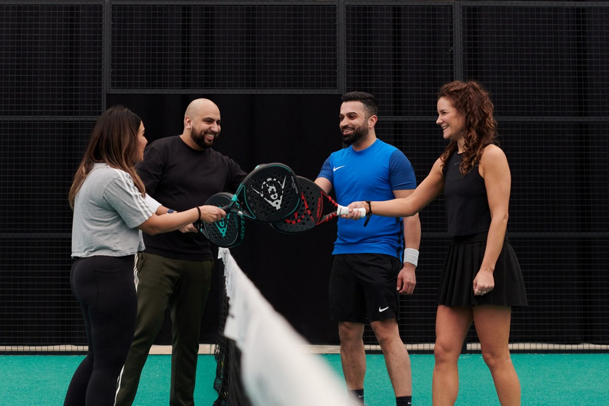 Four padel players laughing together at the net after a social match