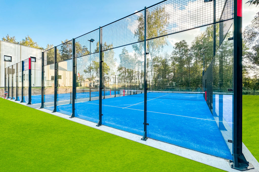 Close-up of a padel court glass back wall with players reflected in the glass during a match