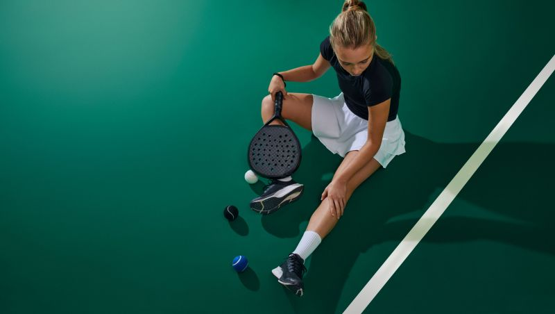 Padel racket, ball, and court shoes viewed from above on a blue padel court surface